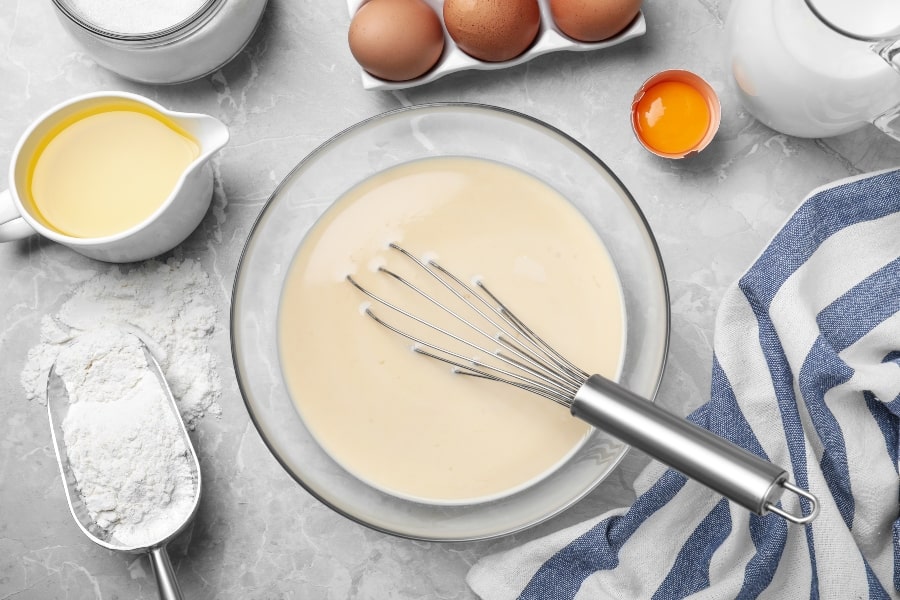pancake batter in bowl with whisk eggs on table