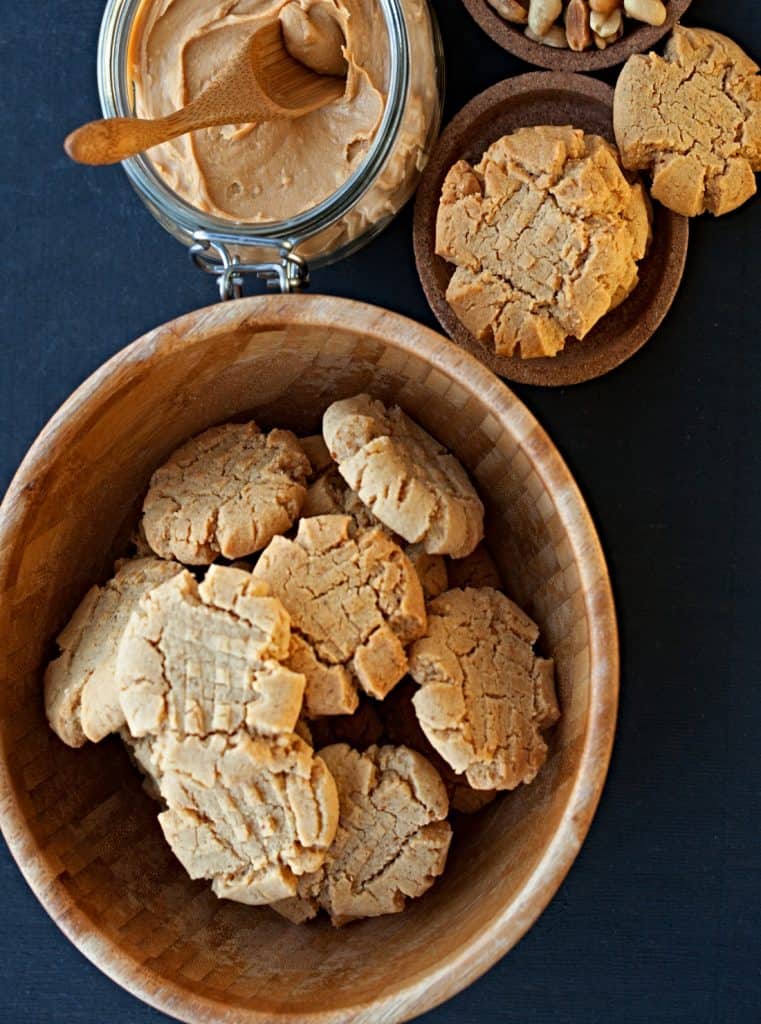 top view of bowl of fresh baked peanut butter cookies with jar of creamy peanut butter