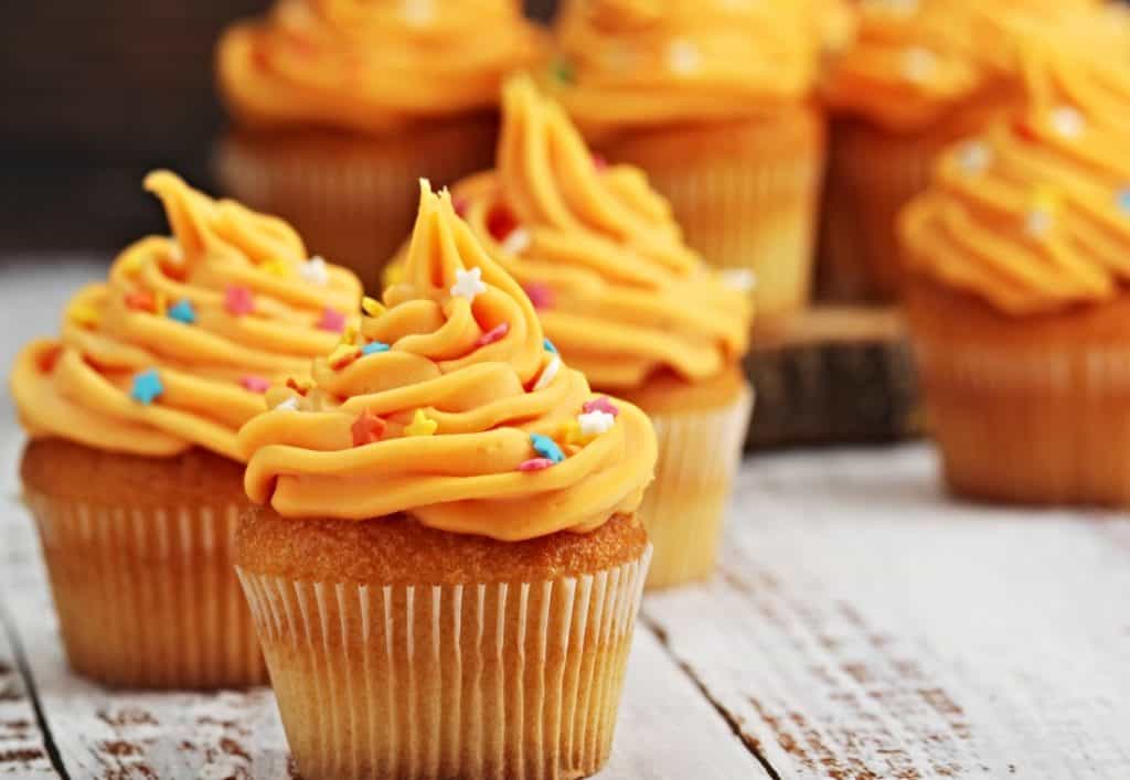closeup of fresh baked cupcakes with orange buttercream frosting and sprinkles