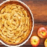 overhead view of deep dish apple pie on wooden table with fresh apples next to it