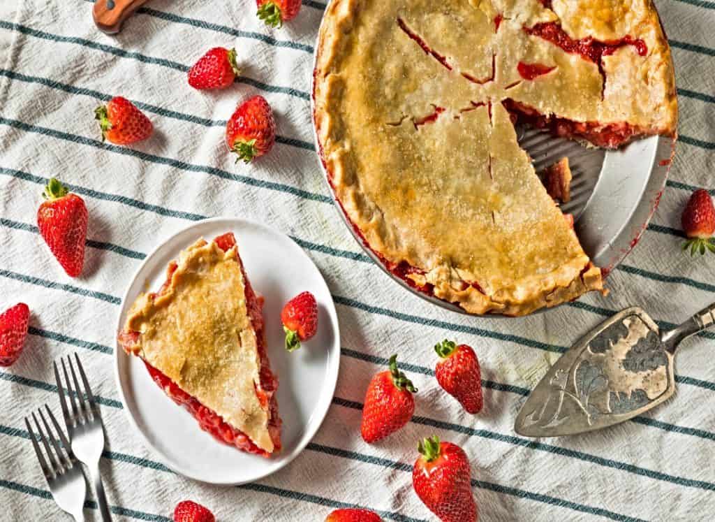slice of strawberry rhubarb on plate and pan with rest of pie all on table