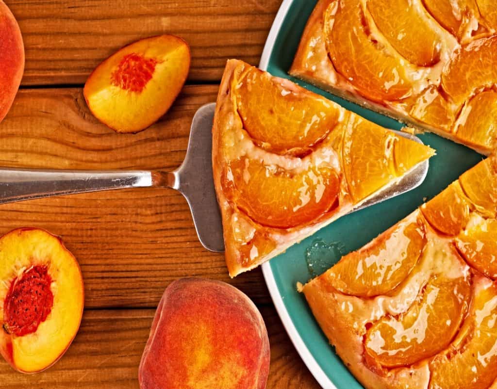 slice of fresh peach pie and whole pie on wood table viewed from above